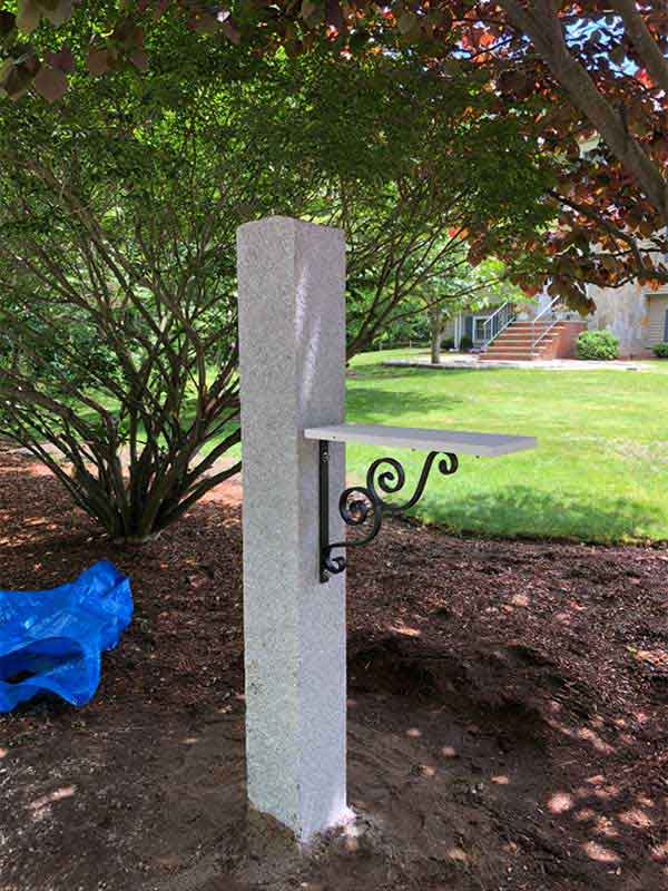 Board for mailbox to sit installed to grey concrete post, with black brackets underneath it