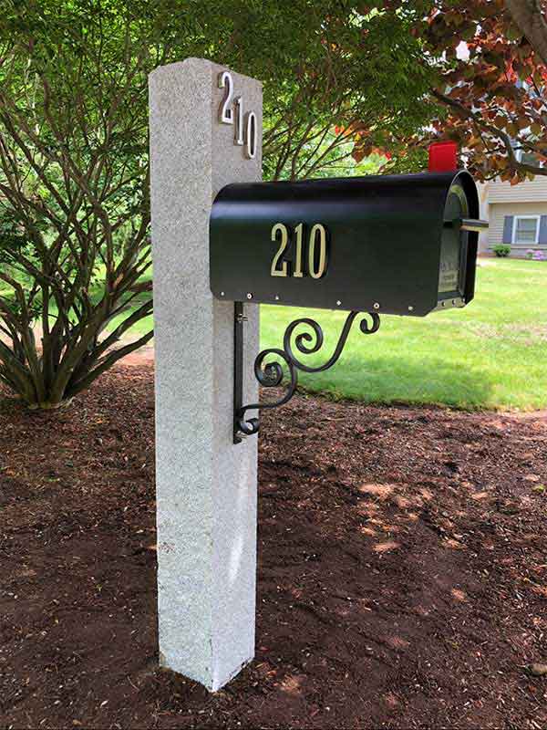 New Black Metal Mailbox with number 210 on side. Fresh dirt and clean landscaping in background